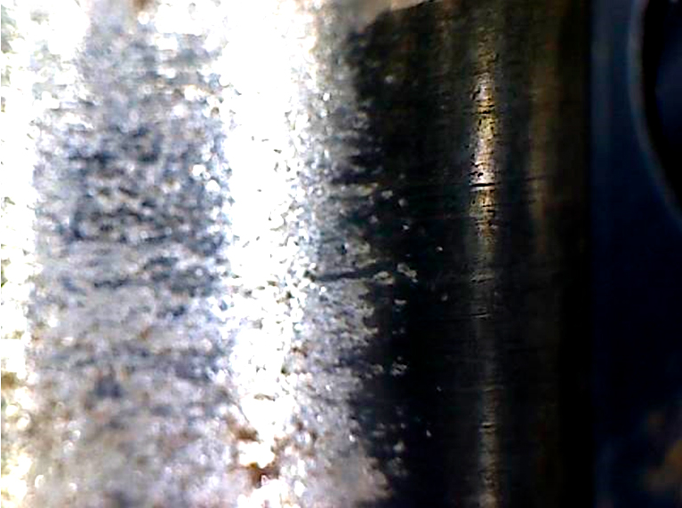 Фото 16. Износ металла и  не повреждённое чёрное антиизносное (антифрикционное) покрытие в месте установки ролика. Вид через микроскоп – увеличение в 10 раз