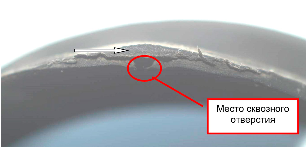 Фото 31. Вид торцевой части в районе трещины и сквозных отверстий. Отсутствие изменения структуры материала резины в виде выкрашивания и  разрушения (показано белой стрелкой). Вид через микроскоп – увеличение в 10 раз.